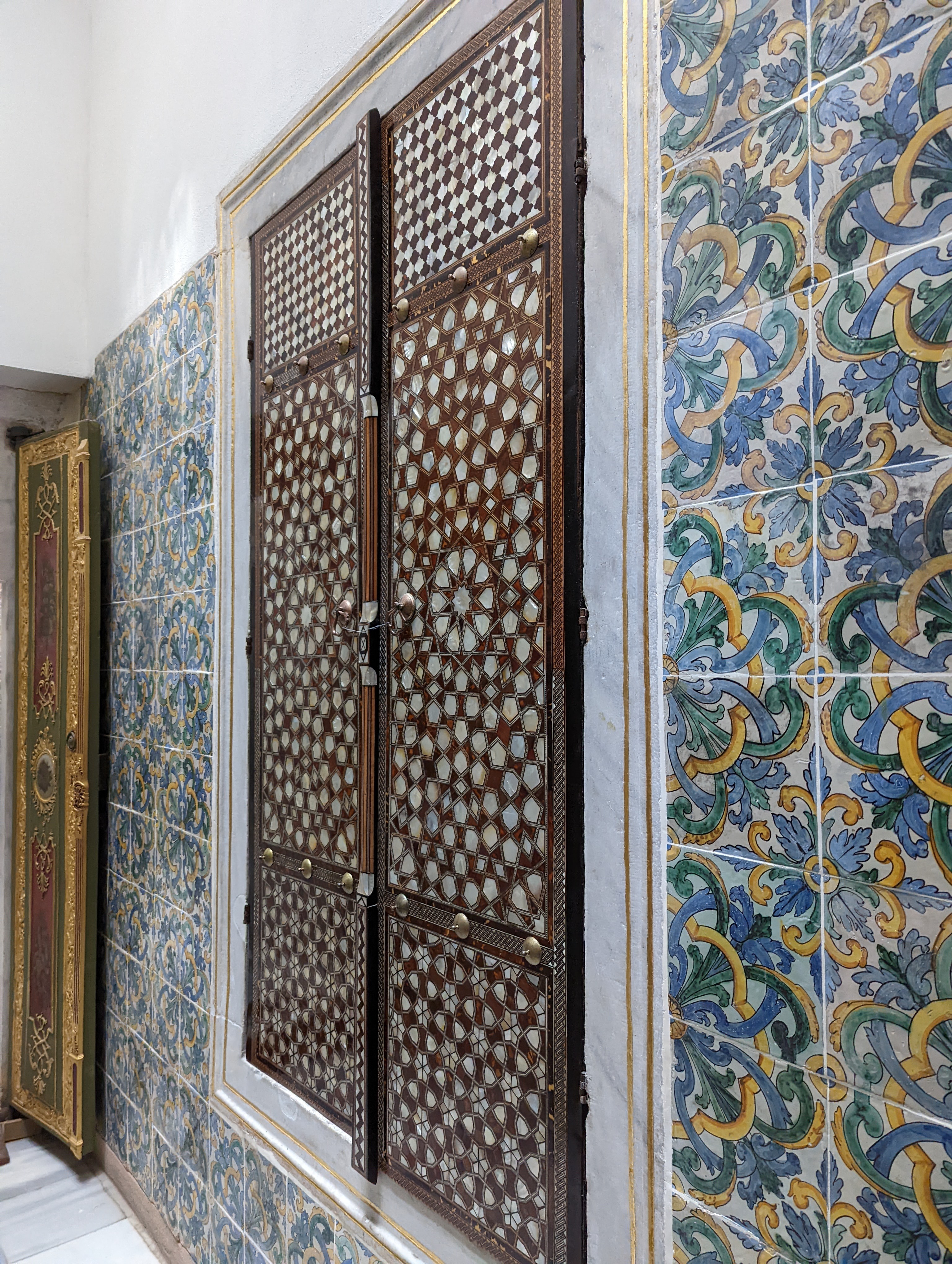 An ornate wall cabinet / shutter door with mother-of-pearl and tortoiseshell inlay, set into the tile-lined corridor walls of the Harem.