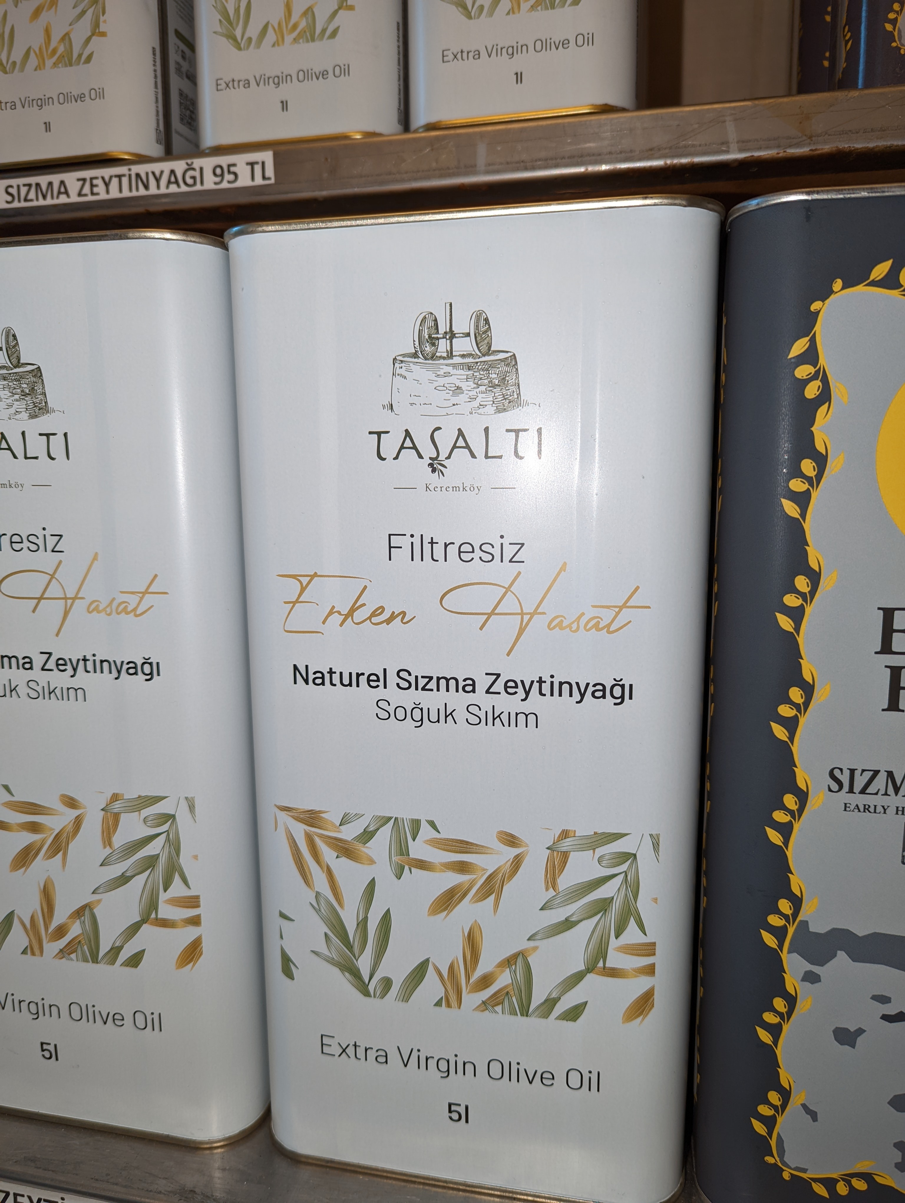 Several large metal cans of Extra Virgin Olive Oil are displayed on a shelf.  oil
