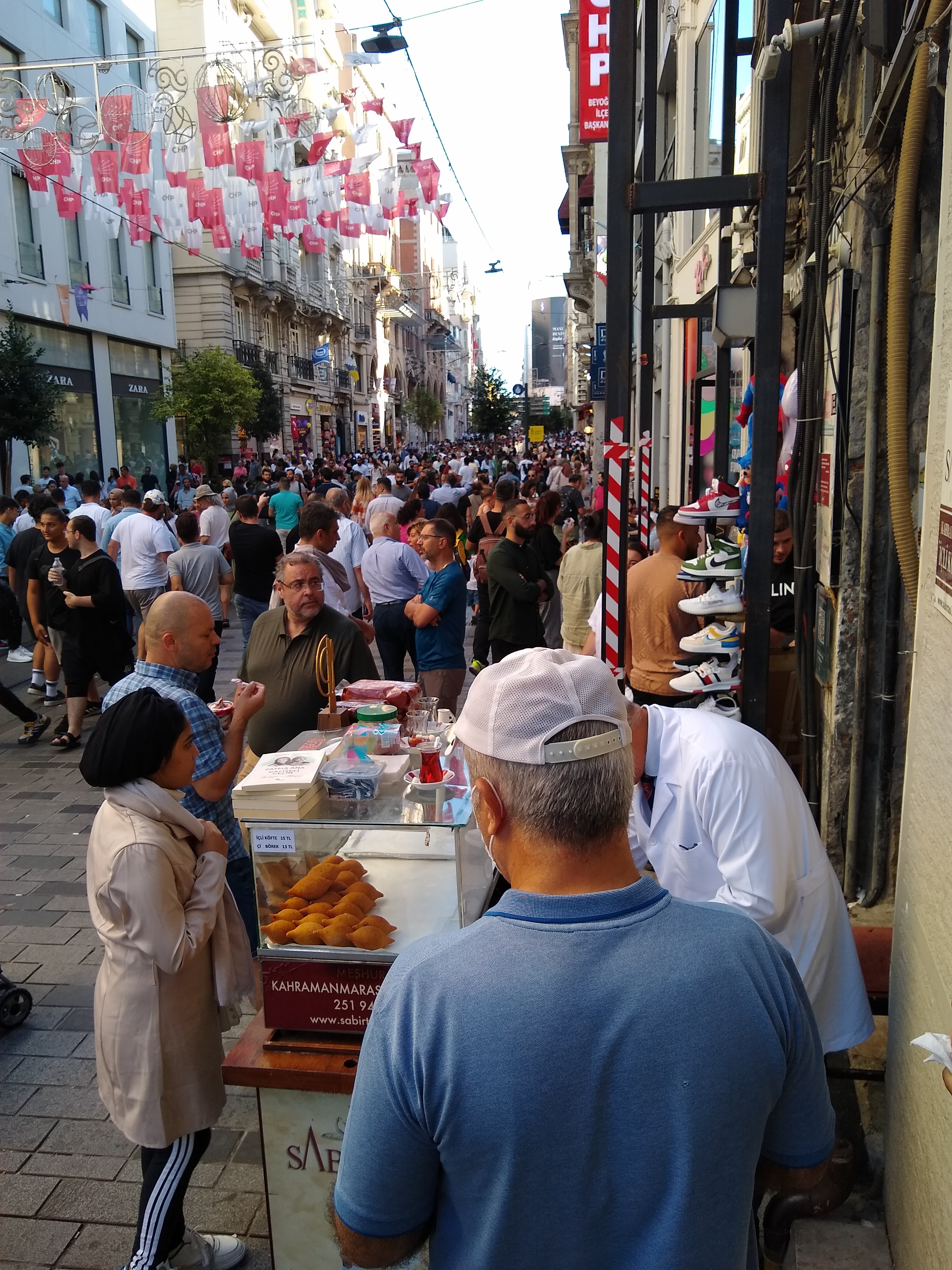 Pedestrians walk past the iconic Sabırtaşı Restoran food cart selling İçli Köftes on İstiklal Avenue near the Beyoğlu Fish Market entrance.