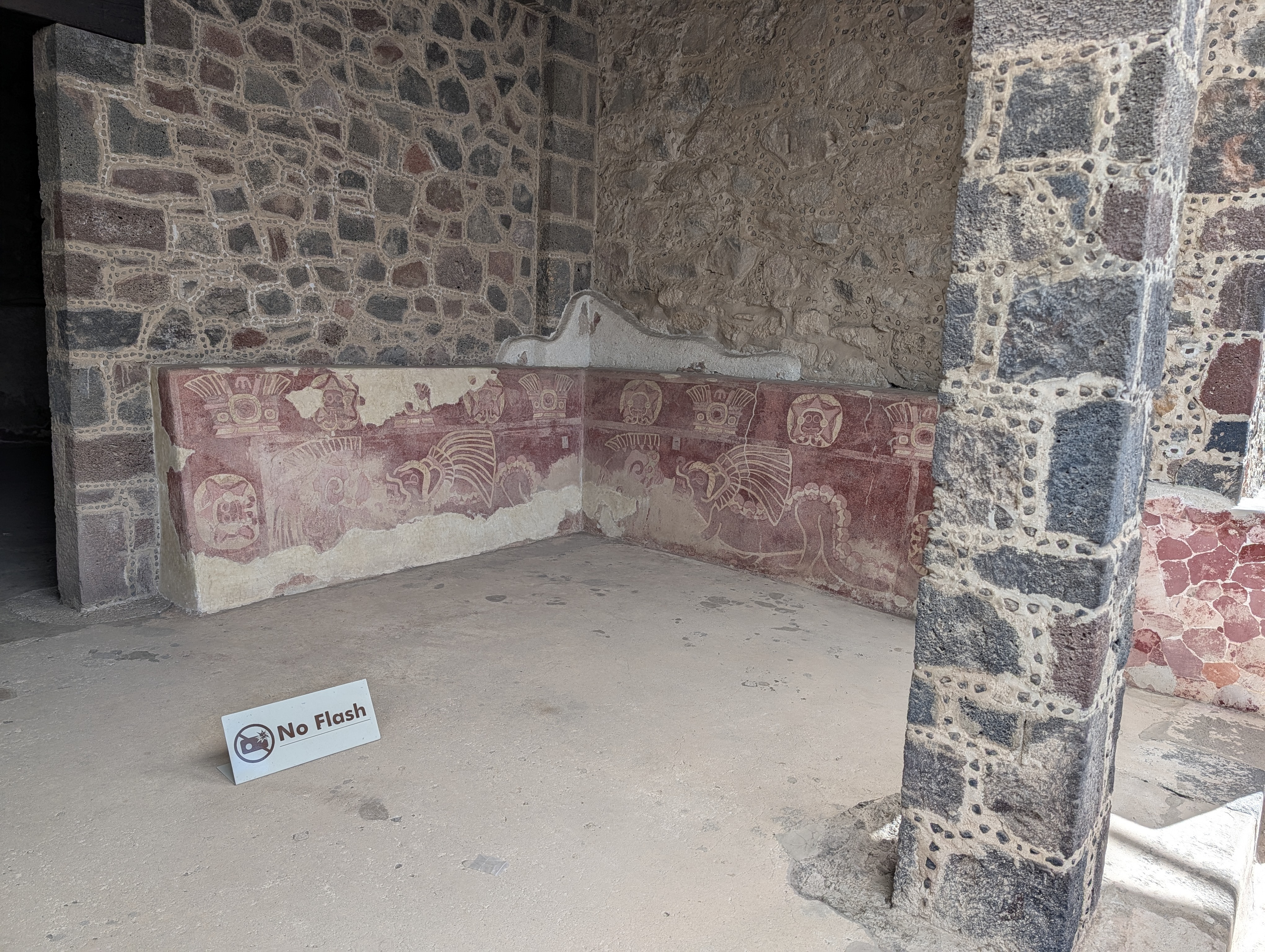 A low painted dado in deep red, capped with a repeating frieze of circular medallions above larger profile figures with elaborate feathered headdresses from one of the residential/ceremonial compounds at Teotihuacán