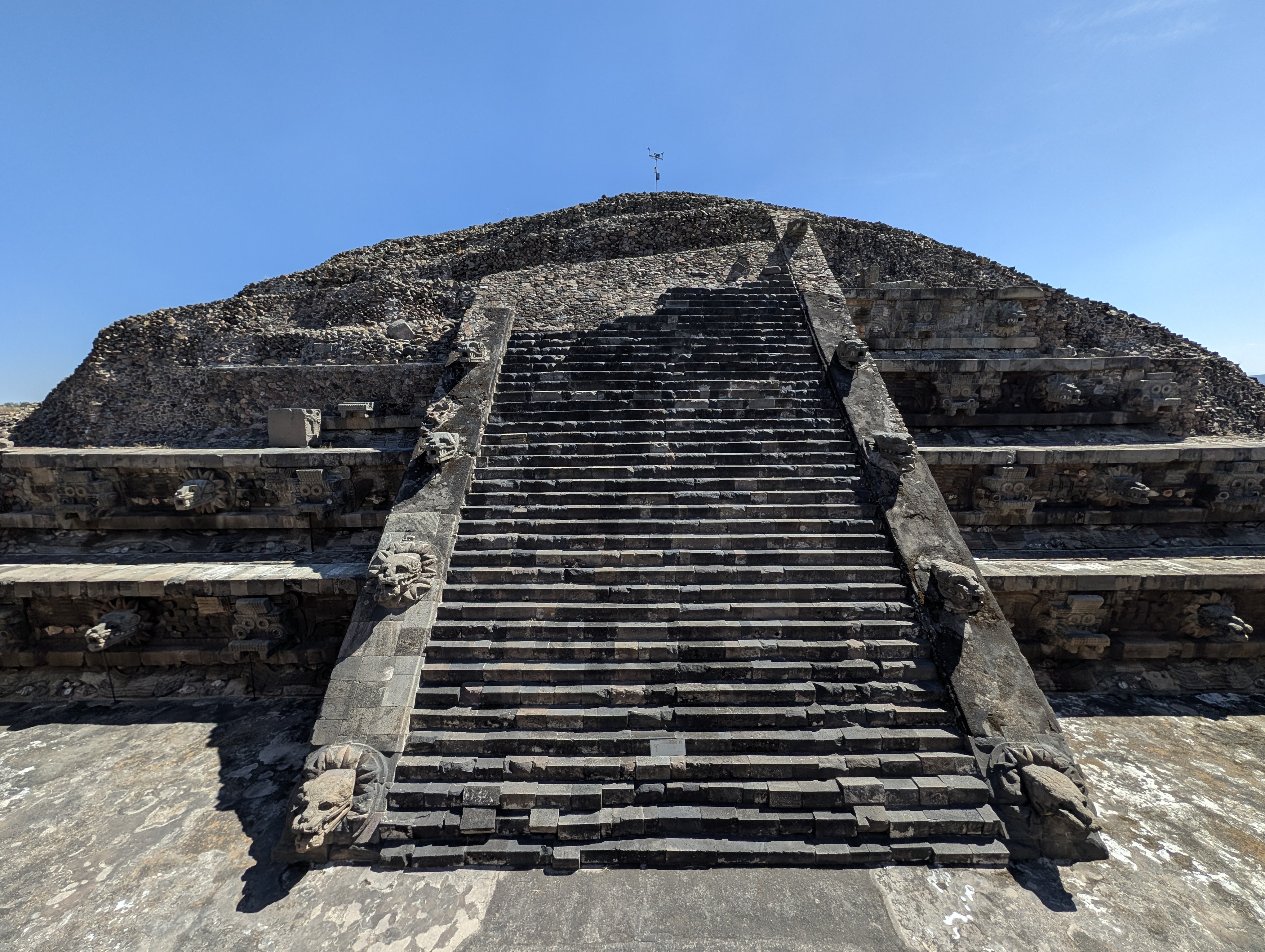 The Temple of the Feathered Serpent (Templo de Quetzalcóatl), seen from the base of its steep central staircase, with the carved serpent-head balustrades flanking the steps.