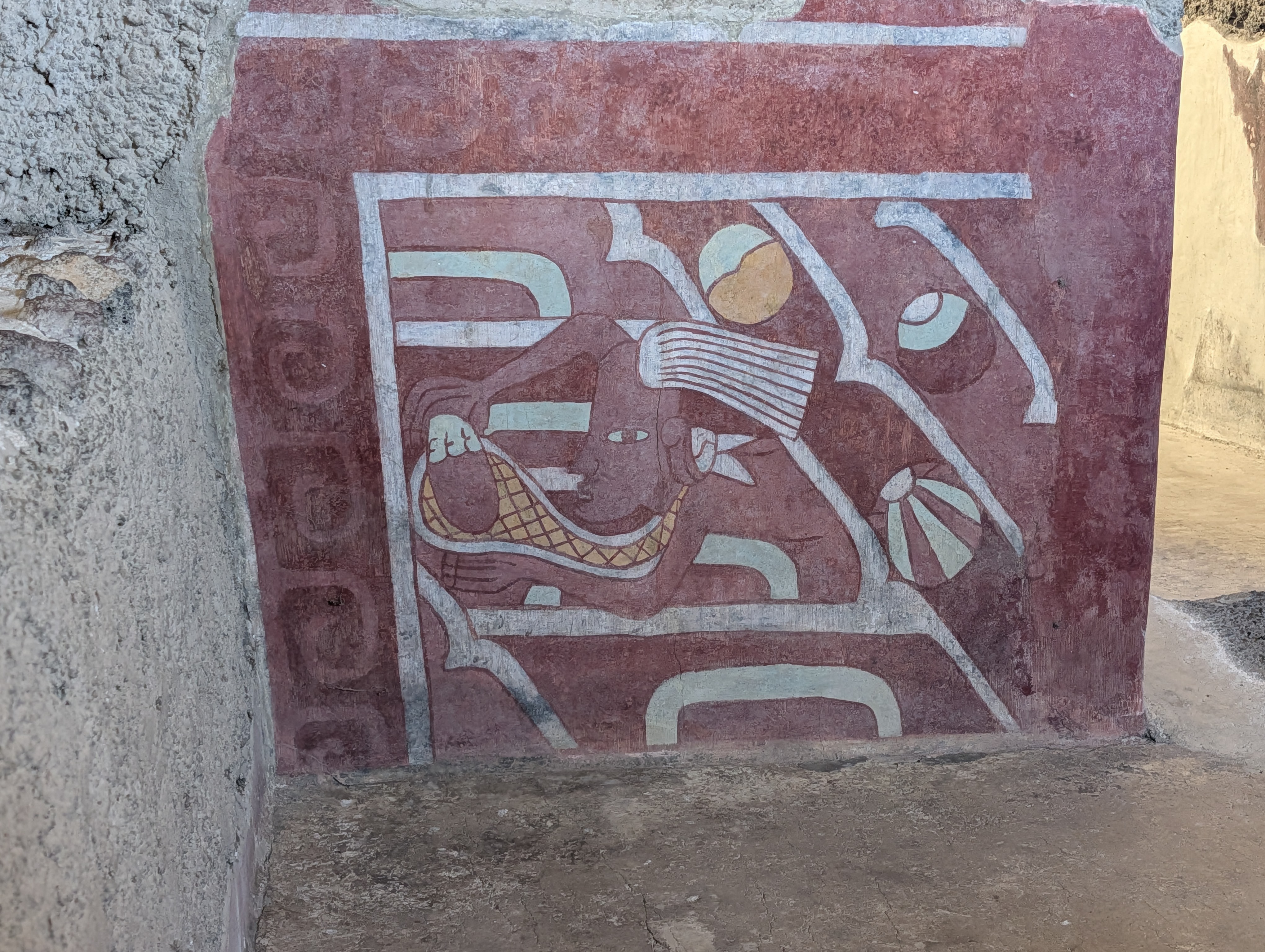 A mural panel from Teotihuacán's Tepantitla compound — the deep red background, the figure with an elaborate feathered/paper headdress, speech scroll (the striped element near the mouth), and the surrounding stepped-fret 