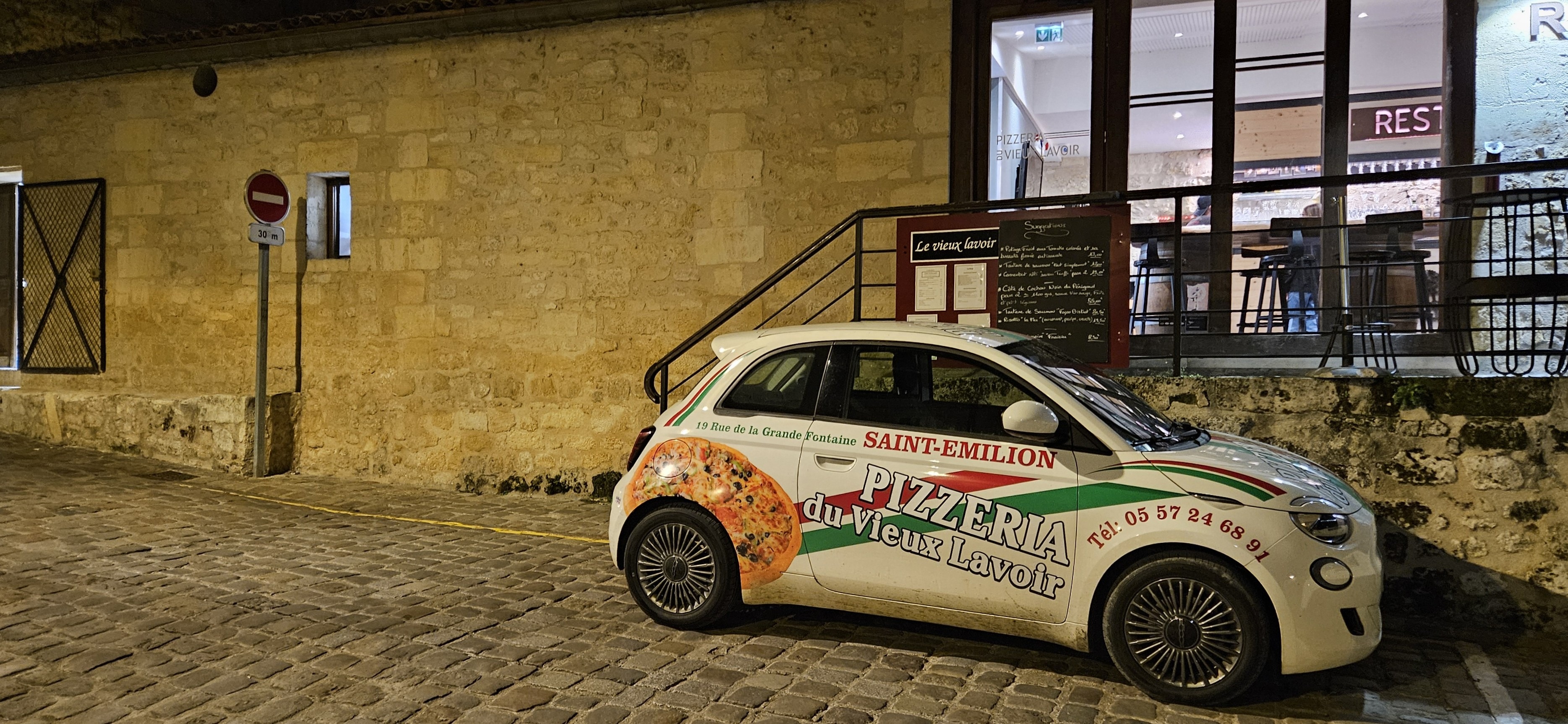 Pizza delivery car on cobblestone street in front of restaurant