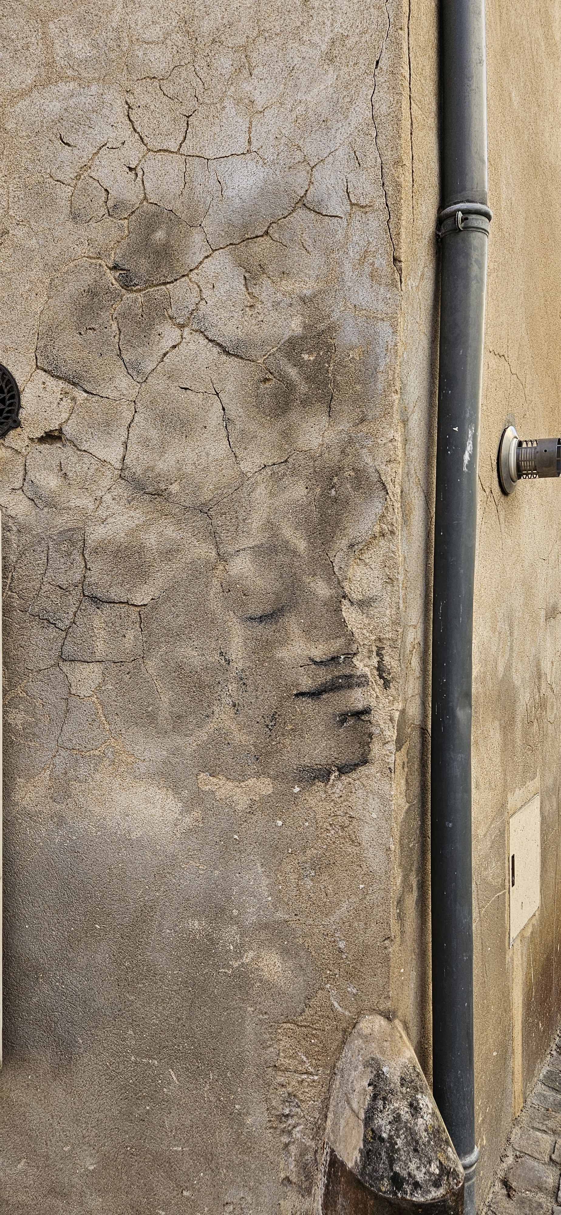 Subtle street art face blending into cracks in stucco