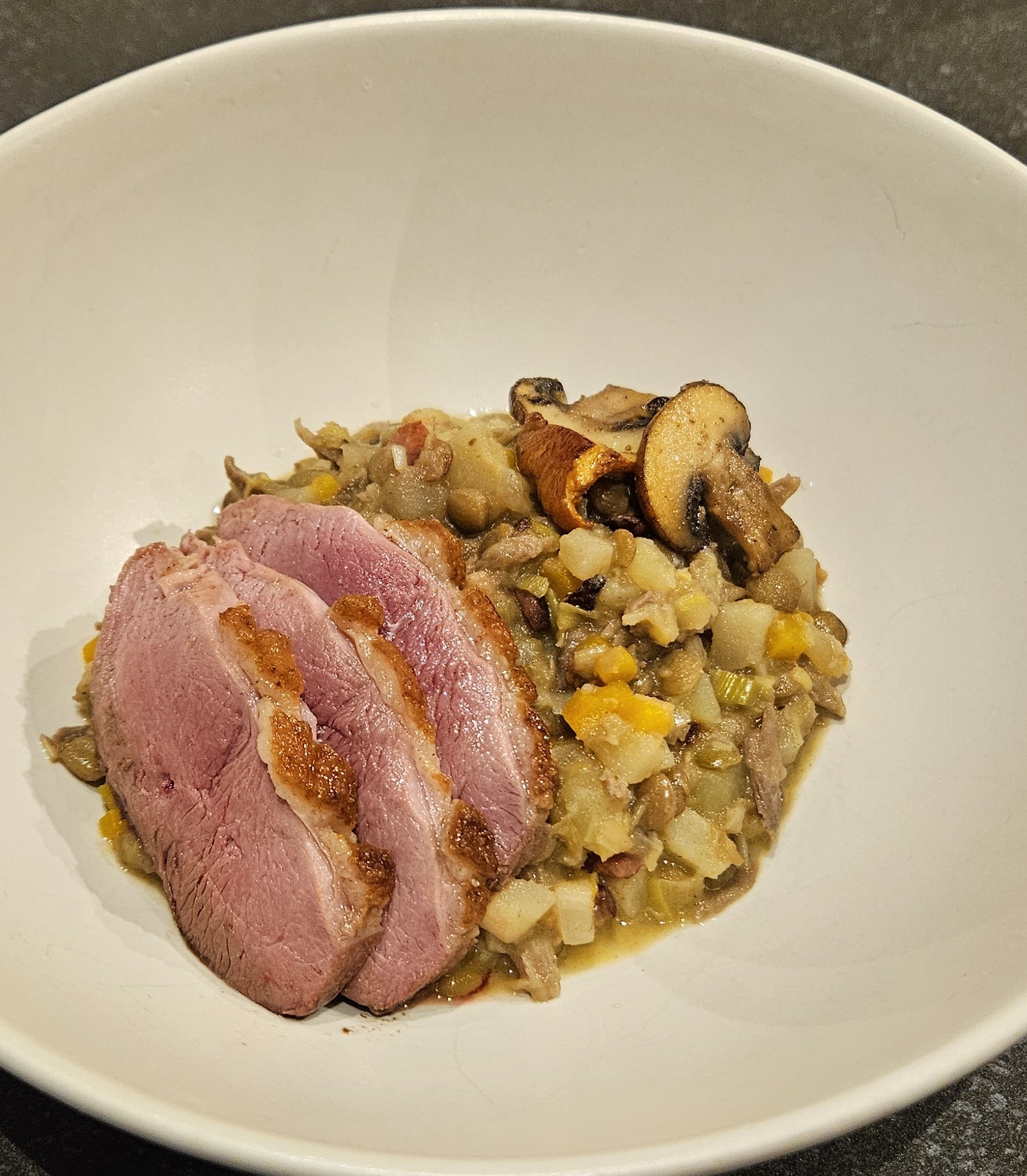 Vegetable, lentil, and duck ragout, topped with sliced duck breast and browned mushrooms
