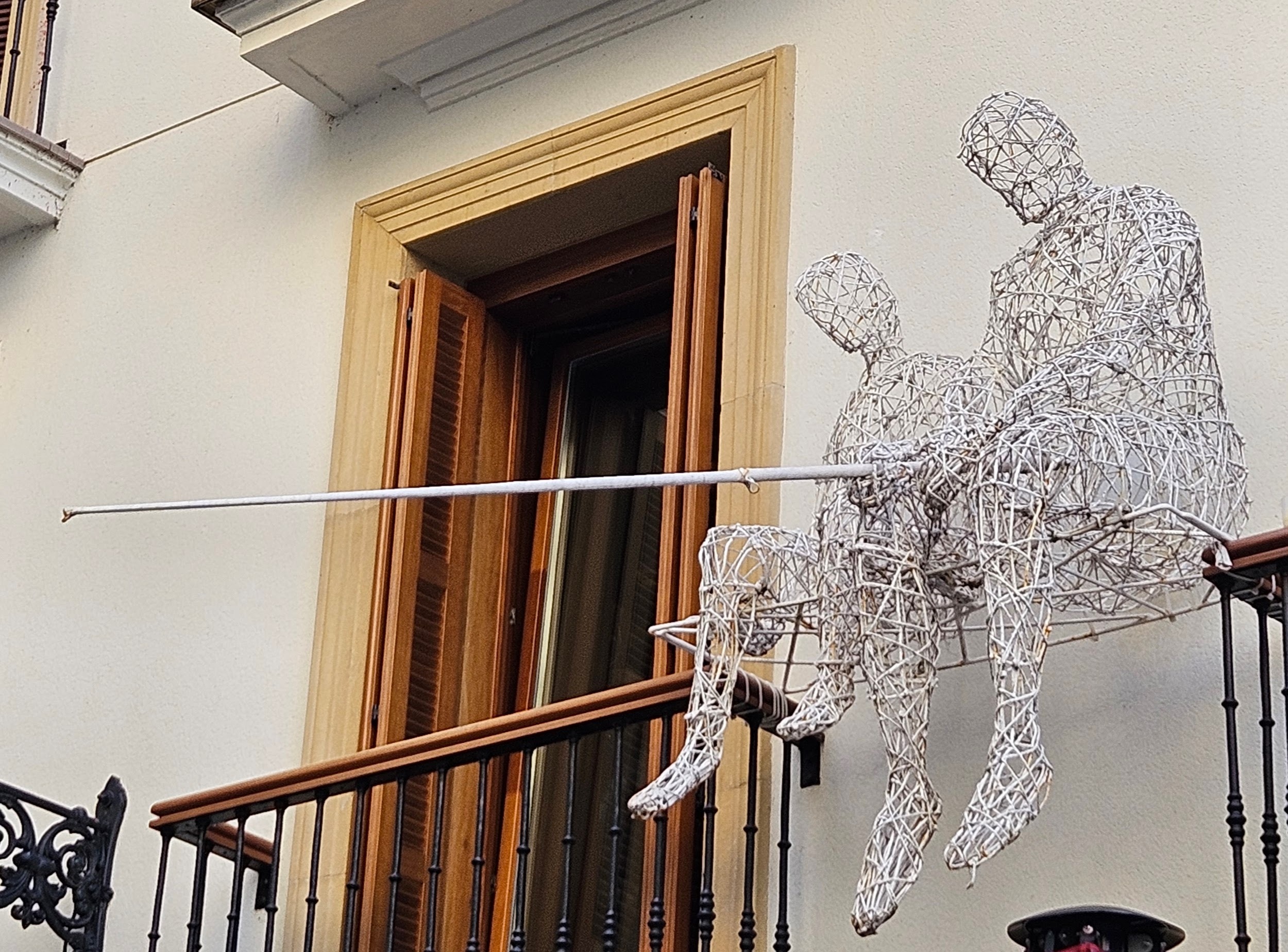 Wire art of people 'fishing' from a balcony